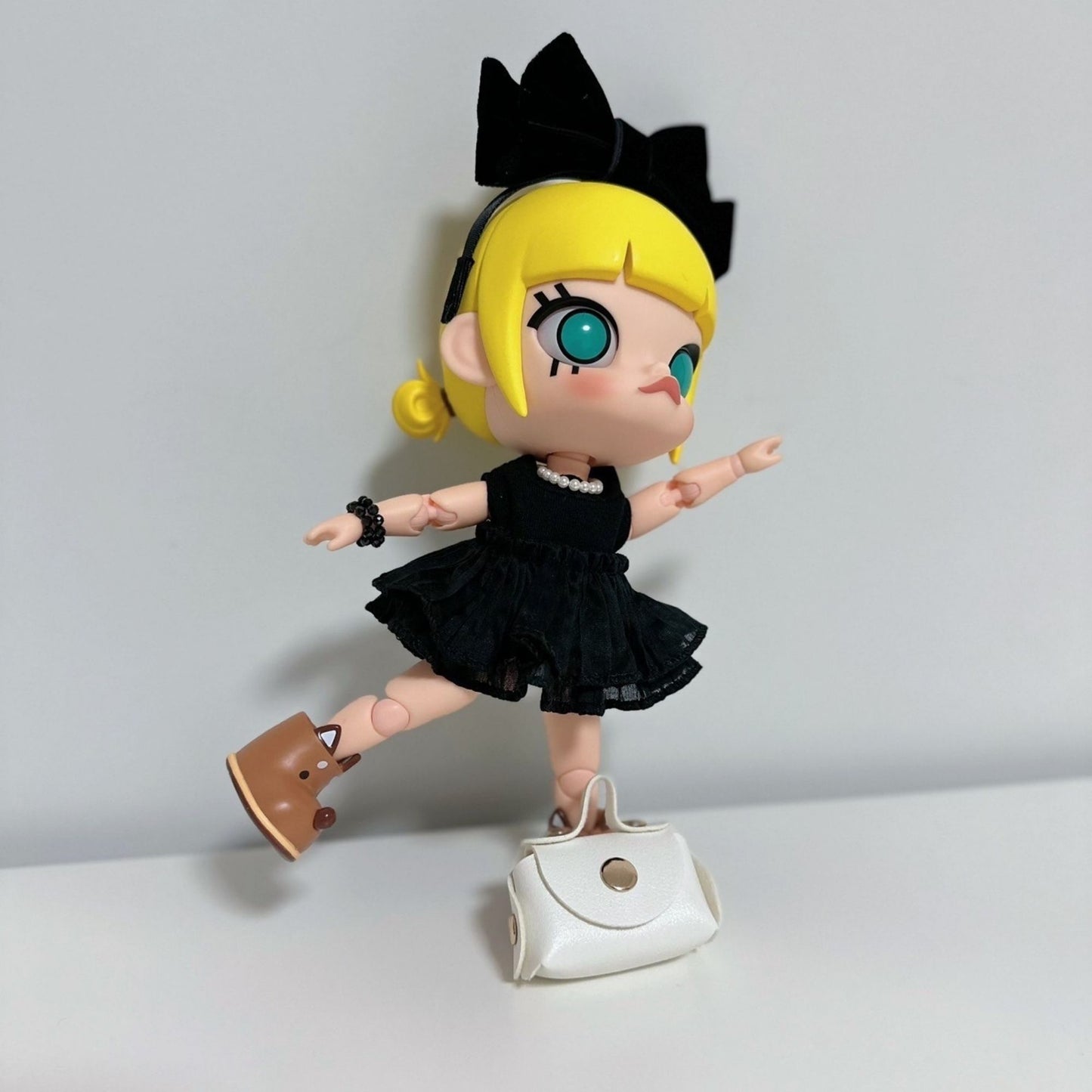 Molly doll wearing a cute black dress with pearl necklace, bow headband, brown shoes, and a white handbag accessory.