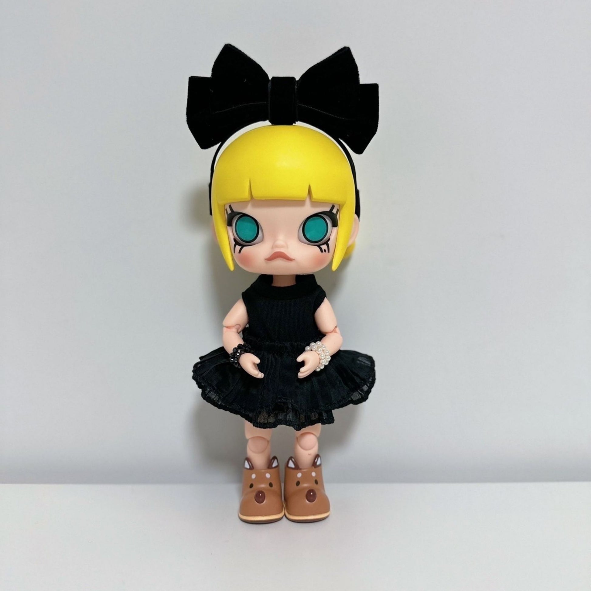 Molly collectible figure wearing a black ruffled dress with lace details, black bow headband, and brown boots. The doll has blonde hair with bangs, large teal eyes, and is posed against a white background
