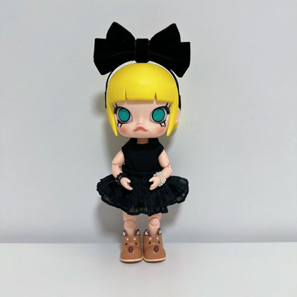 Molly collectible figure wearing a black ruffled dress with lace details, black bow headband, and brown boots. The doll has blonde hair with bangs, large teal eyes, and is posed against a white background