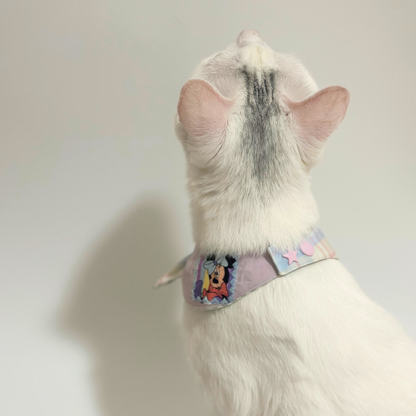 White cat wearing a colorful bib with cartoon characters on a plain background