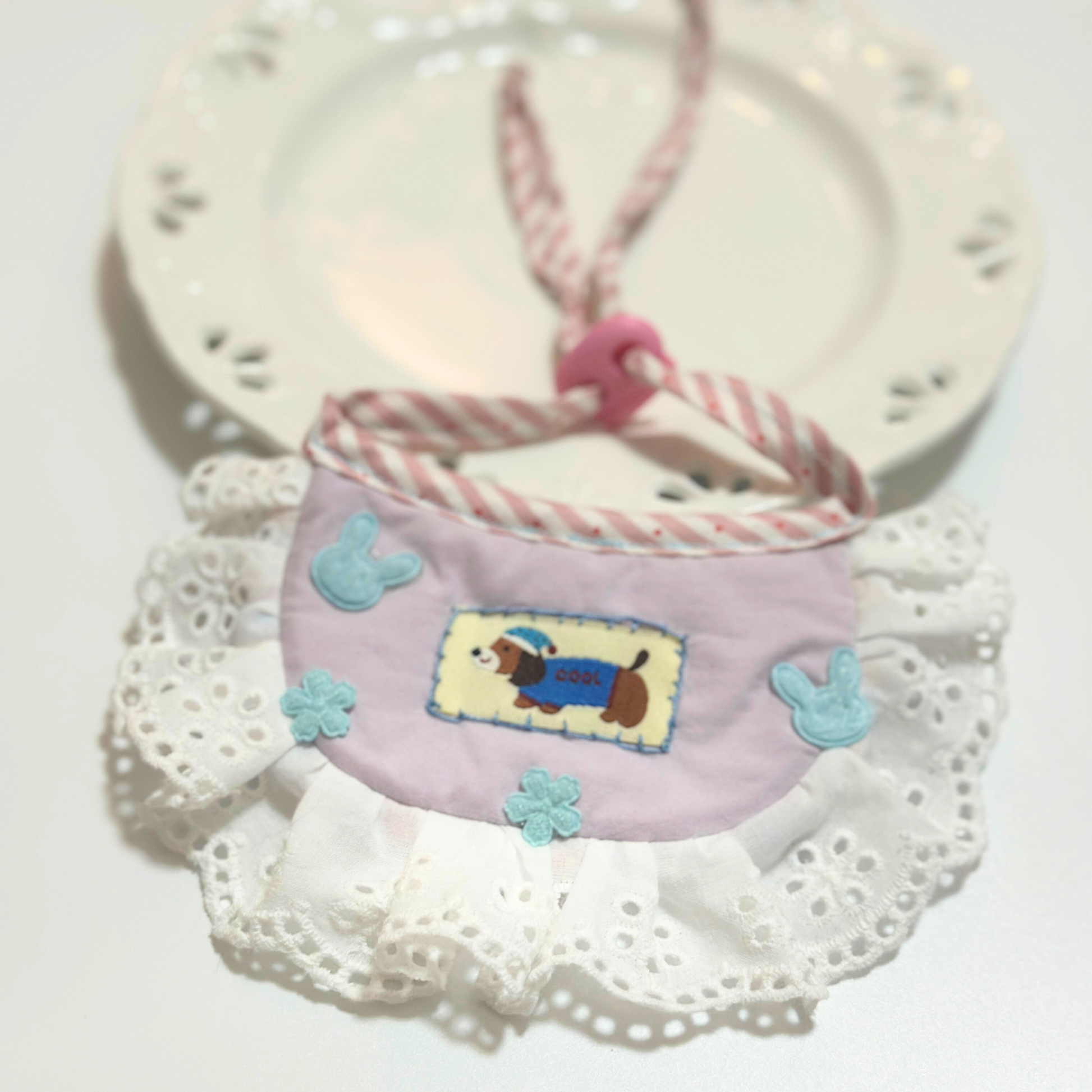 Dog bib bandana lifestyle photo - Pink pet bib with corgi embroidery, bunny decorations, eyelet lace ruffle, displayed with vintage clock for scale and style