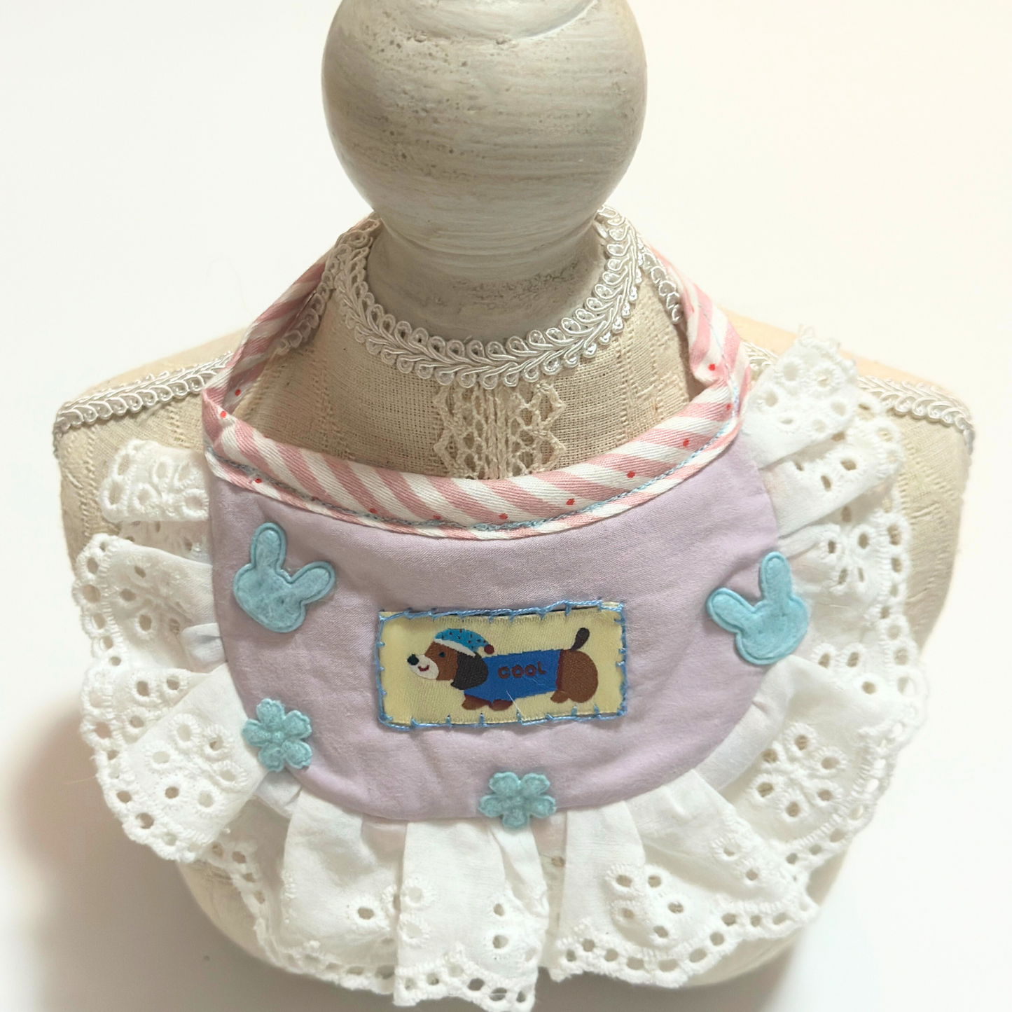 Dog bib bandana with ruffles - Pink pet bib for small dogs displayed on mannequin, featuring embroidered dog design, eyelet lace trim, and adjustable striped ties