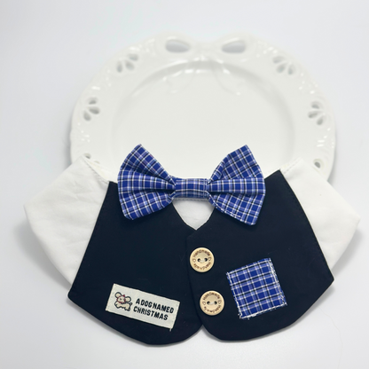Navy blue formal pet bib with white collar and blue plaid bow tie displayed on white ceramic plate with paw print design, featuring "A Dog Named Christmas" label and handmade wooden buttons