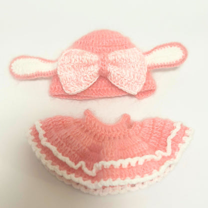 Handmade knitted bunny costume set for Labubu doll laid flat on white background. Top piece shows pink rabbit ears beanie with white bow decoration and long ear flaps. Bottom piece displays matching pink ruffled dress with white scalloped trim and layered design. Complete two-piece coral pink knitted outfit with white accent details.