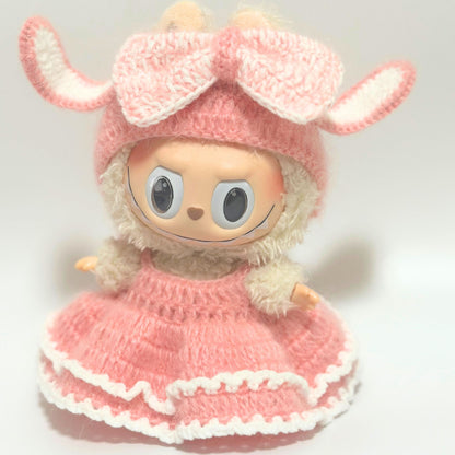 Labubu doll wearing handmade knitted pink bunny costume with white trim. Features adorable rabbit ears hat, fluffy white collar, and layered pink dress with white ruffled edges. The soft knitted outfit transforms the collectible figure into an cute bunny character