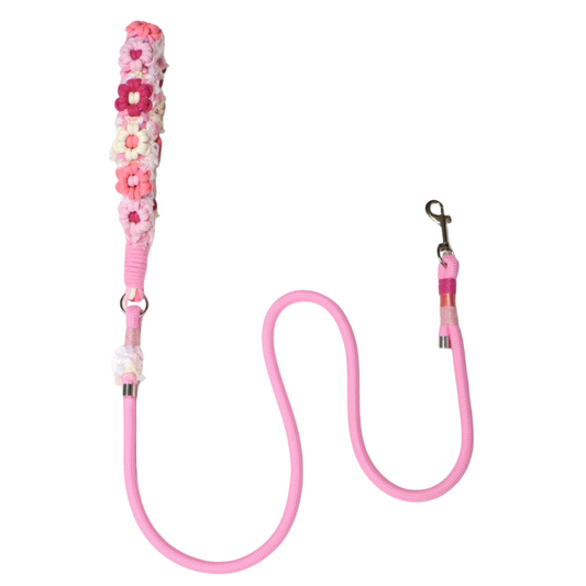 A pink dog leash decorated with artificial flowers in shades of pink, white, and burgundy arranged along the handle, with metal clips on both ends