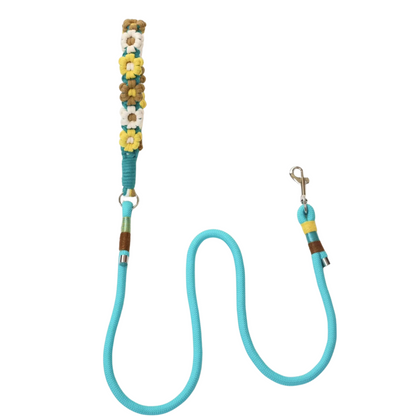 A turquoise dog leash with handle decorated with artificial flowers in yellow, white, brown, and teal colors resembling sunflowers and daisies, featuring metal clips and colorful rope wrapping