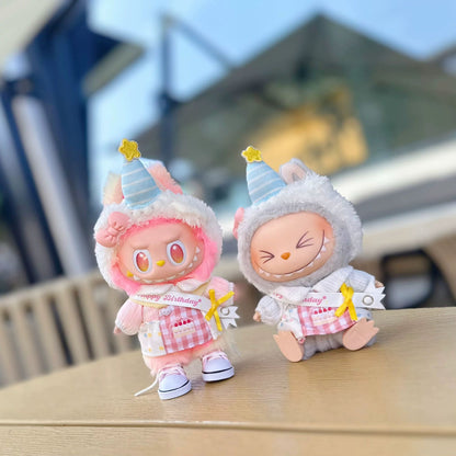Two Labubu plush keychains in birthday party outfits - one pink with happy expression, one grey with sleepy smile, both wearing striped party hats and Happy Birthday sashes